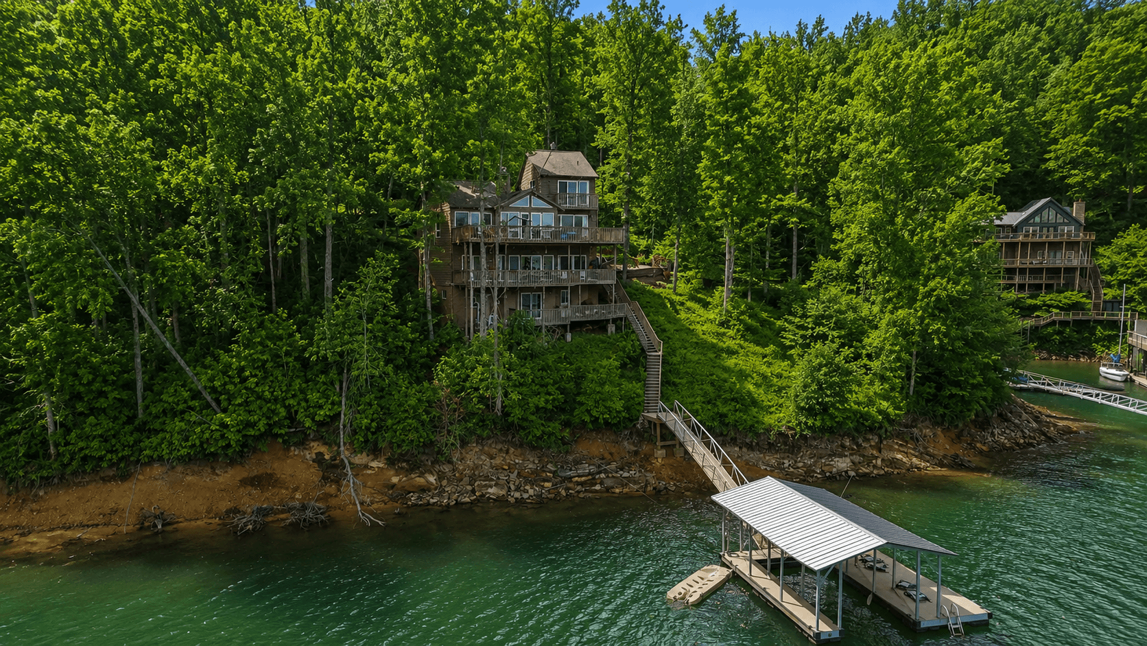 Aerial view of the house on the ridge with the private covered dock below, a jet ski in the slip, and the gangway connecting them.