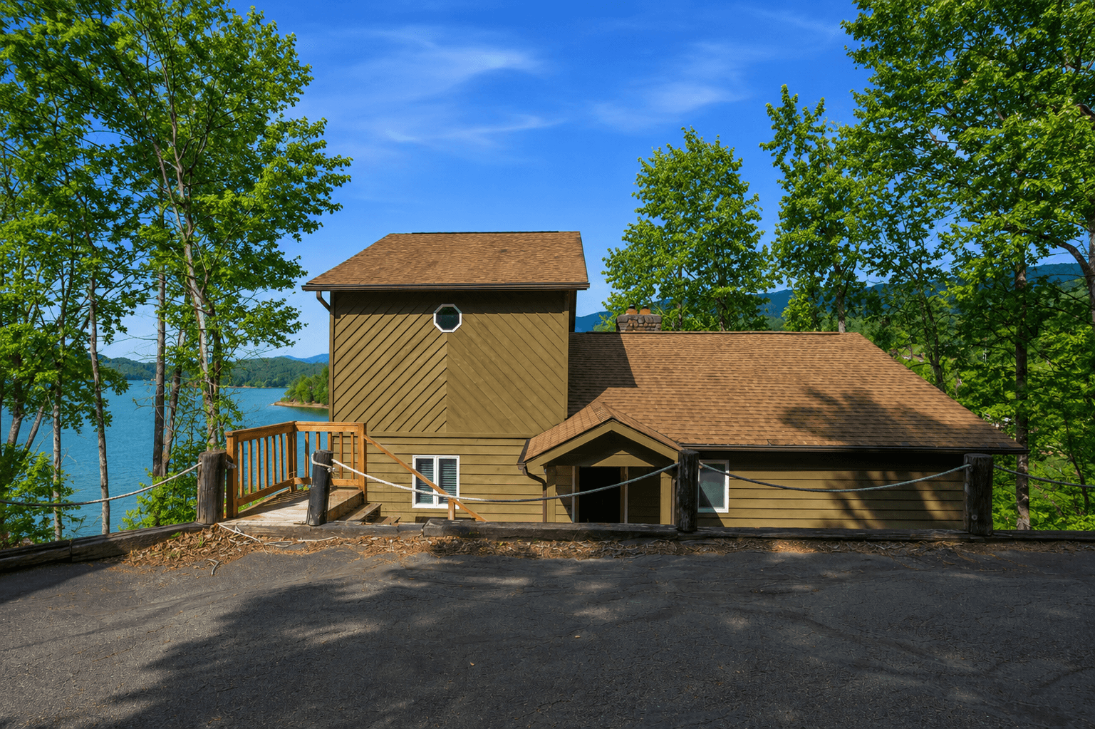 The arrival side of the house from the parking area, with the entry, the deck bridge, and the lake beyond.