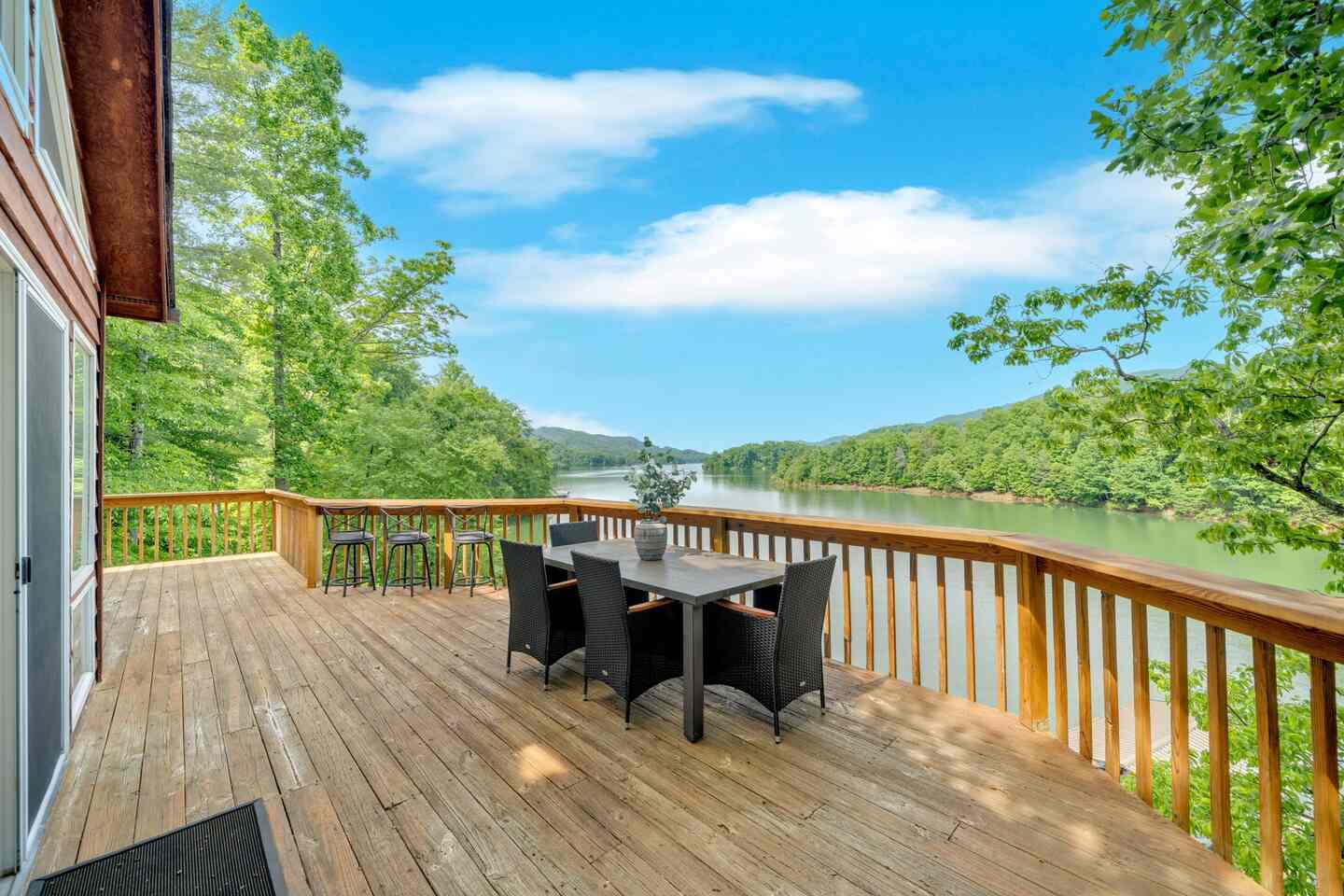 The main deck, with a dining table, bar seating along the rail, and the lake and ridgelines beyond.