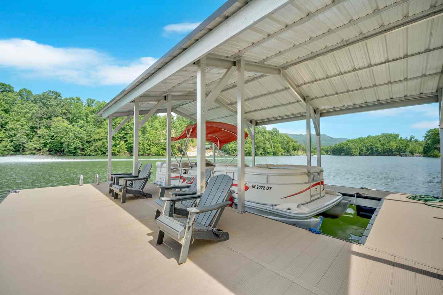 On the dock: the covered slip with a pontoon boat moored, and Adirondack chairs on the open deck alongside.