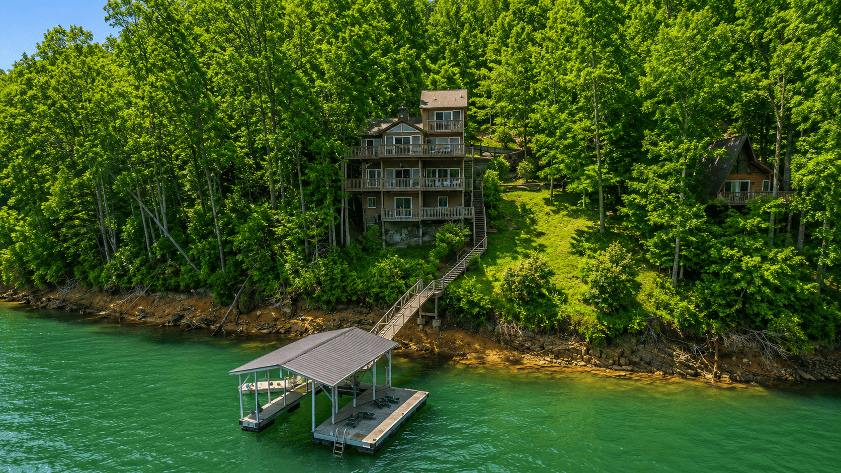 The house seen from the water — decks, the stair run down the hillside, the gangway, and the covered dock with its swim platform and ladder.